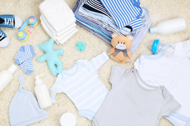 Baby clothes with toys and diapers on carpet - Foto, Imagen
