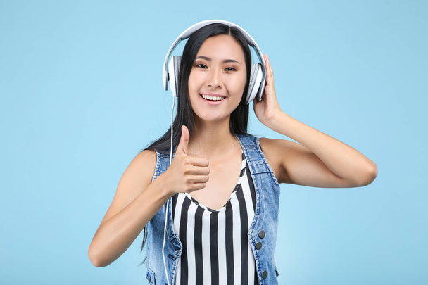 Beautiful woman with headphones showing thumb up on blue backgro - Фото, изображение