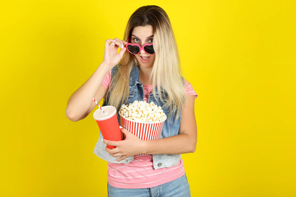 Young woman in sunglasses holding bucket with popcorn and paper  - 写真・画像