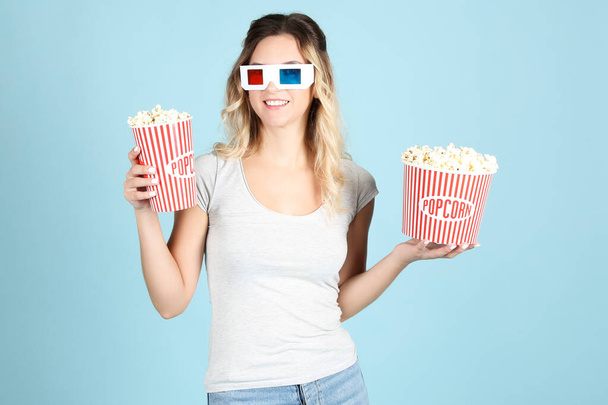 Young woman in glasses holding buckets with popcorn on blue back - Foto, Imagem