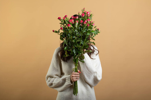 Immagine di una giovane bella donna che posa isolata contro un muro arancione con in mano un mazzo di rose rosa
 - Foto, immagini