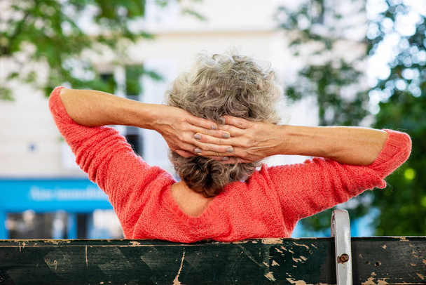 Retrato por detrás de una mujer de mediana edad sentada en el banco con las manos detrás de la cabeza
 - Foto, Imagen