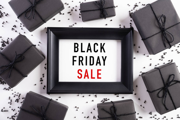 Top view of Black Friday Sale text on white picture frame with black gift box and Christmas ball and berries on white background. Shopping concept and black Friday composition. - Φωτογραφία, εικόνα