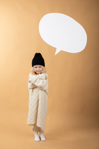 A girl in a hat stands on an orange background and shows emotions - Foto, afbeelding