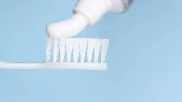 Zahnpasta auf eine Bürste auf blauem Hintergrund auftragen - Filmmaterial, Video