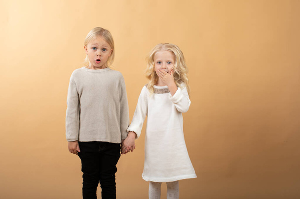 Egy kislány fehér kötött ruhában, fekete kalapban és egy fiú pulóverben. Kezet tartó gyermekek - Fotó, kép