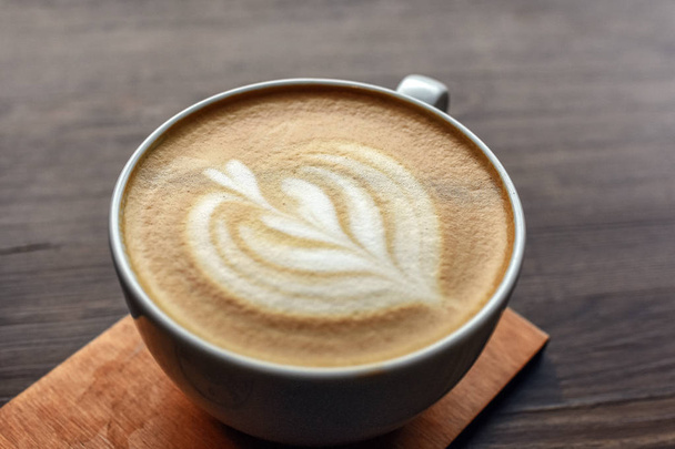 Nahaufnahme einer Tasse Kaffee auf einem Holztisch mit Herzmuster darauf. Selektiver Fokus. - Foto, Bild