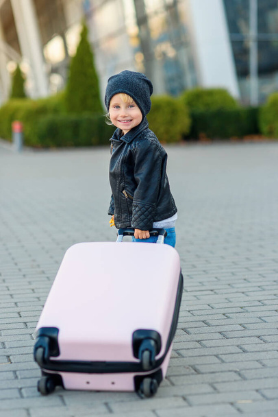 Cute little traveler girl pulls pink suitcase towards the airport. - Фото, изображение