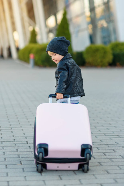 Cute little traveler girl pulls pink suitcase towards the airport. - Фото, изображение