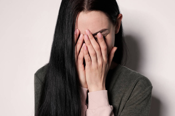 Upset young woman crying against light background - Φωτογραφία, εικόνα