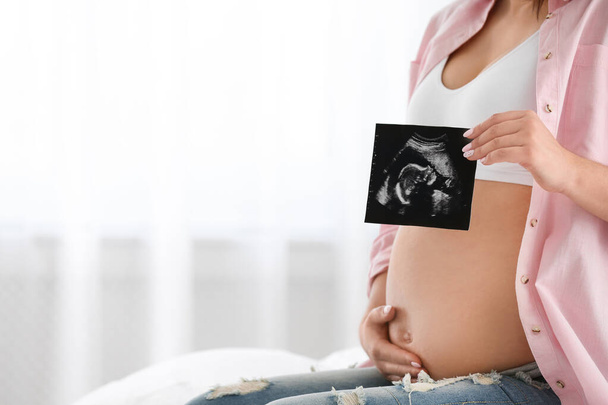 Pregnant woman with ultrasound picture indoors, closeup. Space for text - Фото, изображение