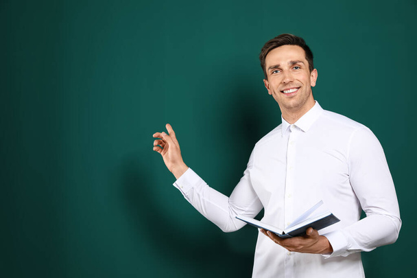 Portrait of male teacher with book on color background. Space for text - Foto, afbeelding