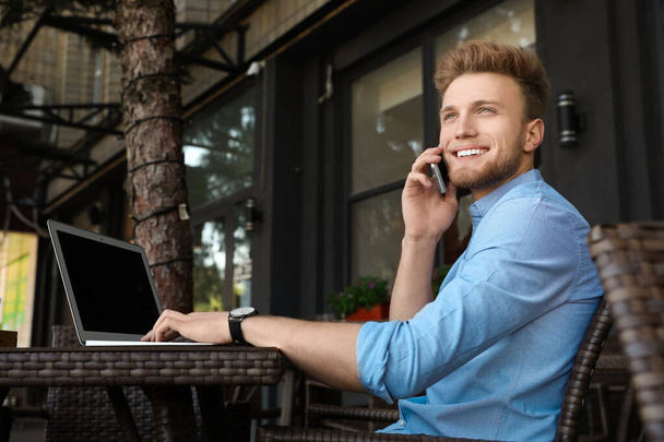 Bello giovane uomo con computer portatile seduto a tavola in caffè all'aperto
 - Foto, immagini