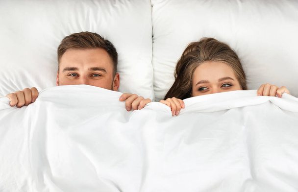 若いカップルが一緒に毛布の下に隠れて、トップビュー。就寝時間 - 写真・画像