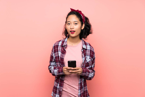 Азійська молода жінка через ізольований рожевий фон здивована і відправляє повідомлення - Фото, зображення
