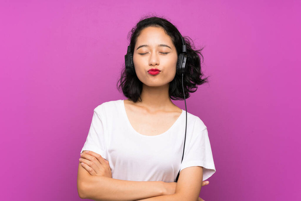 Asian young girl listening music with a mobile over isolated purple wall - Fotoğraf, Görsel