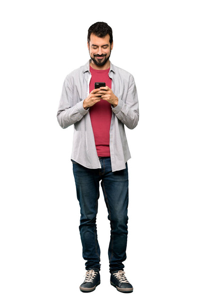 Teljes hosszúságú lövés a jóképű férfi szakállal küld egy üzenetet a mobil elszigetelt fehér háttér - Fotó, kép