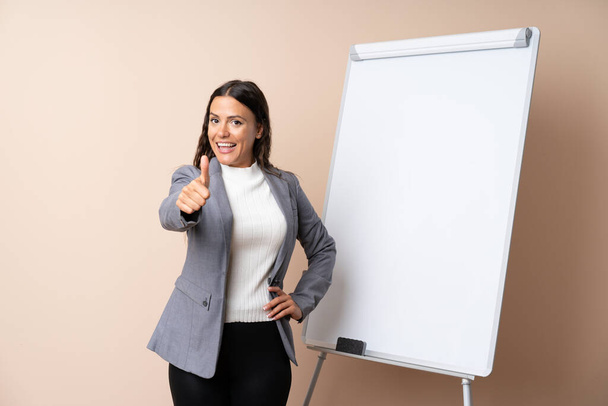 Jonge vrouw geeft een presentatie op wit bord geeft een presentatie op wit bord met duim omhoog - Foto, afbeelding
