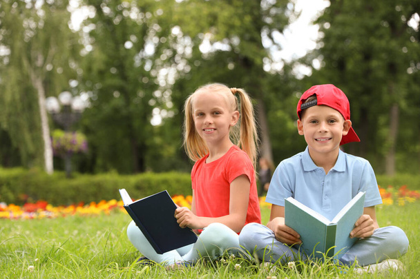 Χαριτωμένα μικρά παιδιά που διαβάζουν βιβλία για το πράσινο γρασίδι στο πάρκο - Φωτογραφία, εικόνα