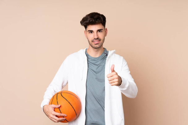 Young man over isolated background playing basketball and with thumb up - Foto, Imagem
