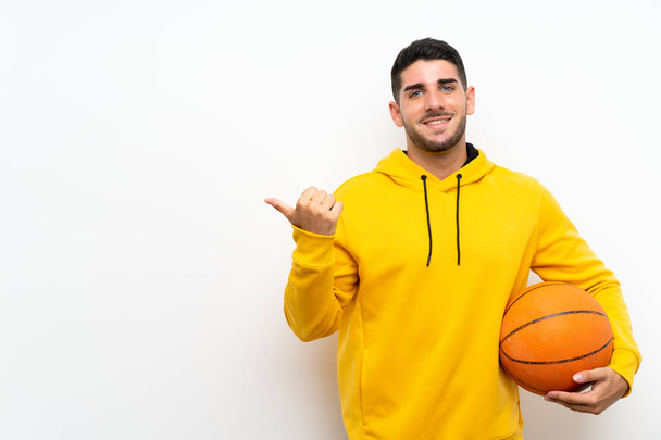 schöner junger Basketballspieler über isolierte weiße Wand, die zur Seite zeigt, um ein Produkt zu präsentieren - Foto, Bild