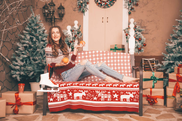 okouzlující hubená dívka v módních džínách vyšívané s perlami a vánoční svetr bosý sedí na lavičce, plná délka těla - Fotografie, Obrázek
