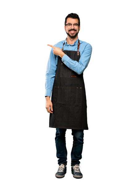 Full-length shot of Man with apron pointing to the side to present a product over isolated white background - Foto, Bild