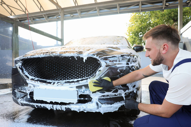 Young worker cleaning automobile with sponge at car wash - Foto, afbeelding