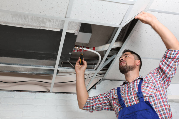 Professional technician repairing ceiling mounted air conditioner indoors - Photo, Image
