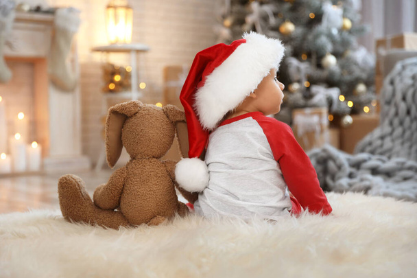 Little baby with Santa hat and toy on floor at home. First Christmas - Foto, afbeelding