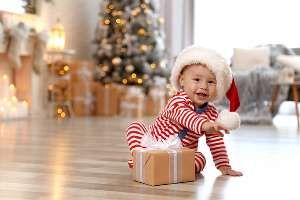 Little baby with Santa hat and Christmas gift on floor at home - Foto, immagini