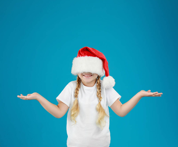 Cute little child wearing Santa hat on blue background. Christmas holiday - Zdjęcie, obraz