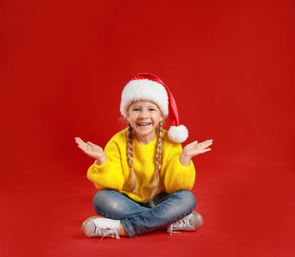 Cute little child wearing Santa hat on red background. Christmas holiday - Valokuva, kuva