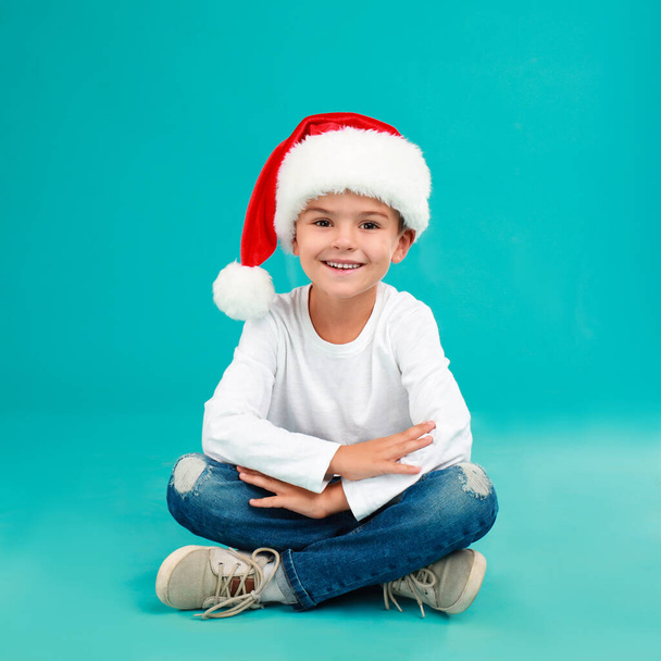 Cute little child wearing Santa hat on light blue background. Christmas holiday - Foto, afbeelding