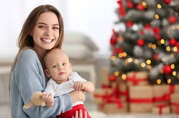 Happy mother with cute baby in room decorated for Christmas holiday - Fotó, kép