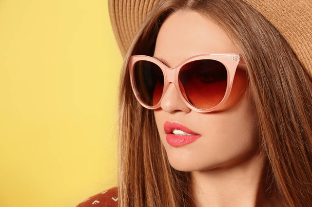 Young woman wearing stylish sunglasses and hat on yellow background - Fotoğraf, Görsel