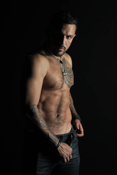 Άνθρωπος με σχεδιασμό τατουάζ στο δέρμα. Γενειοφόρος άνδρας shirtless με fit κορμό. Μόδα μοντέλο δερμάτινη ζώνη αγκράφα στο τζιν. Αθλητής με έξι pack και ab. γυμναστηρίου Αθλητισμός και περιποίηση σώματος - Φωτογραφία, εικόνα
