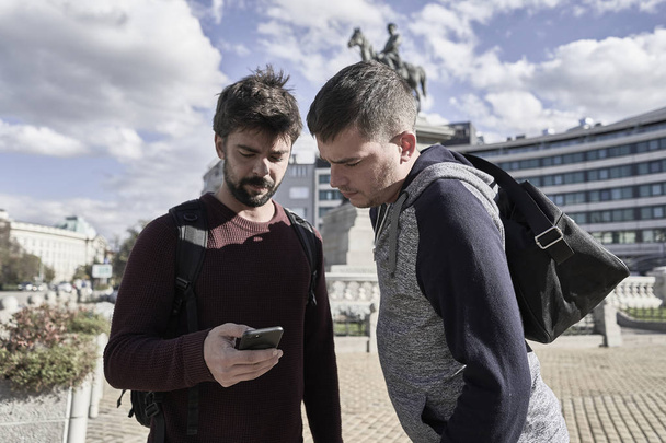 Dois jovens turistas olhando seus celulares em Sofia. Bulgária
 - Foto, Imagem