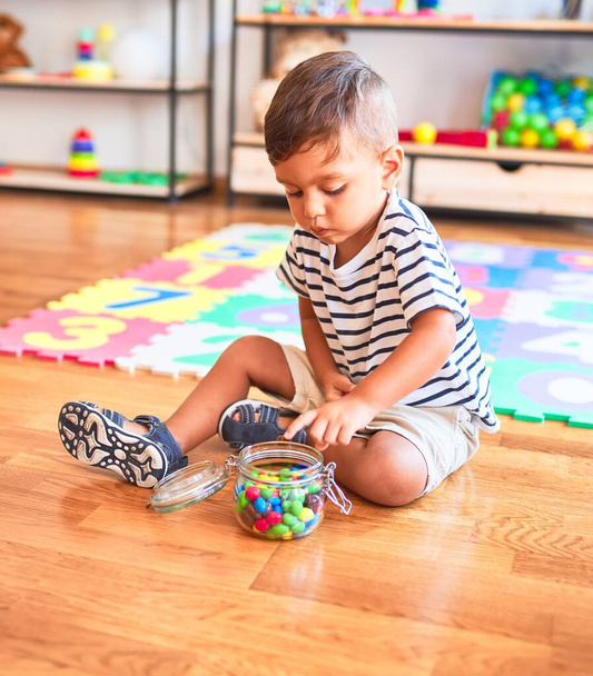 Beau tout-petit garçon assis sur le puzzle manger de petites boules de chocolat de couleur à la maternelle
 - Photo, image