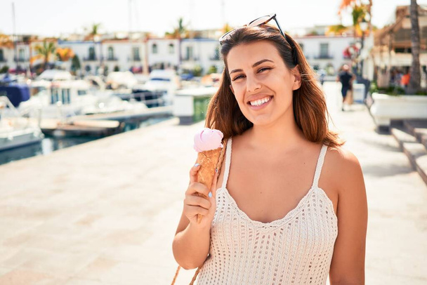 Young beautiful woman eating ice cream cone on a sunny day of summer on holidays - Photo, Image