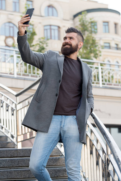 Hand selfie. Bearded man take selfie with smartphone outdoor. Businessman smile to selfie camera in mobile phone. Enjoying selfie session in business style. Modern life - Foto, Imagem