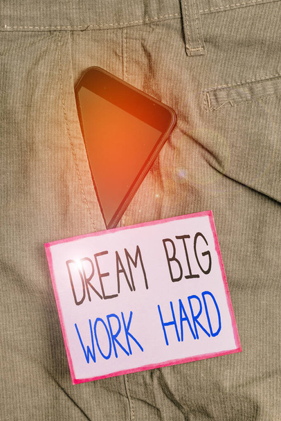 Текстовий знак із зображенням Dream Big Work Hard. Концептуальна фотографія Повірте в себе і слідуйте мріям і цілям пристрою смартфона всередині офіційних робочих штанів передня кишеня біля нотатки паперу
. - Фото, зображення