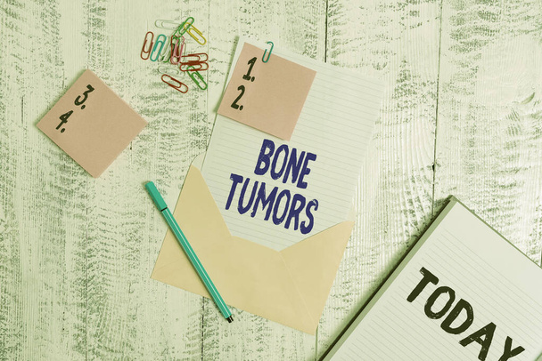 Word writing text Bone Tumors. Business concept for can be either benign or malignant growths found in the bone Envelope sheet paper sticky notes ballpoint notepad clips wooden background. - Photo, Image