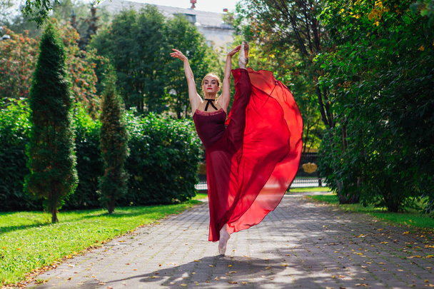Woman ballerina in red ballet dress dancing in pointe shoes in autumn park. - Fotoğraf, Görsel