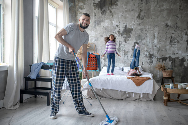Man cleaning the bedroom while daughters having fun - Foto, afbeelding