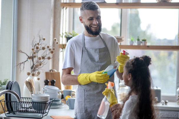 Beaming father taking detergents while cleaning kitchen with daughter - Foto, Bild