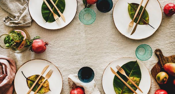 Fall, Autumn table setting for holiday dinner. Flat-lay of dinnerware with fruit and leaves over linen tablecloth, top view, copy space, wide composition. Preparation for Thanksgiving day or Christmas - Фото, изображение