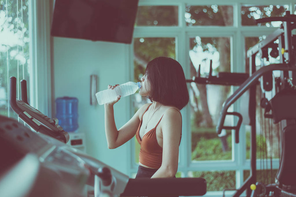 Slim woman sitting and drinking water in gym,Asian female break and relax after workout - Valokuva, kuva