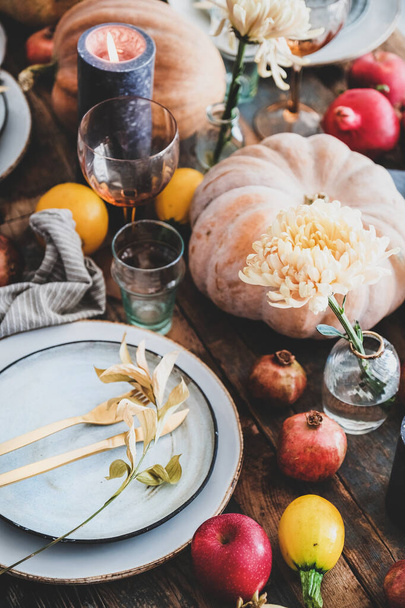 Fall table setting for Thanksgiving day or family gathering dinner. Plates, silverware, floral and fruits decoration, candles and pumpkins over rustic wooden table background, close-up - 写真・画像