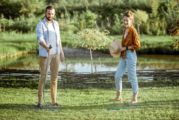 Mann und Frau gießen grünen Rasen im Hinterhof - Foto, Bild